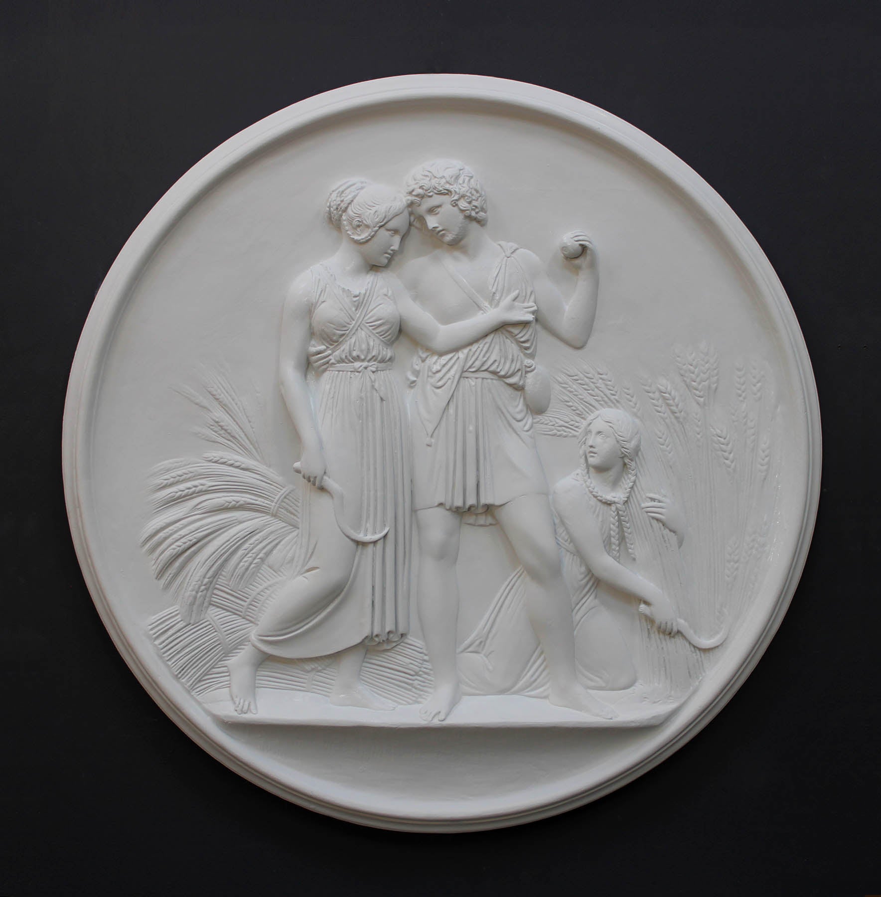 photo of white plaster cast relief sculpture of male and female figures walking through field of wheat and a female figure kneeling in the field cutting wheat against dark gray background