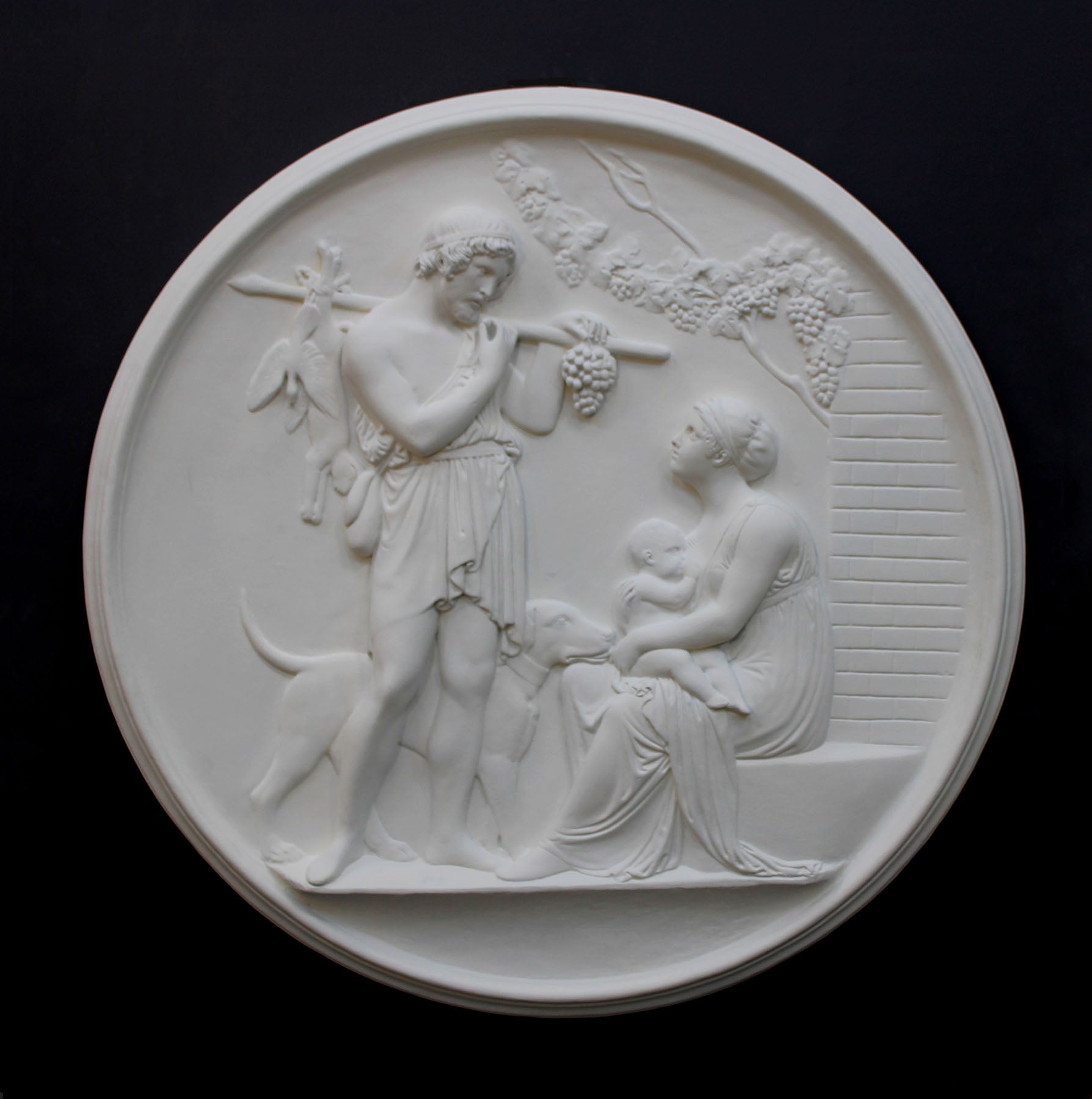 photo of white plaster cast relief sculpture of female figure with baby on lap, a standing male figure, and a dog against dark gray background