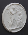 photo of white plaster cast relief sculpture of female figure with baby on lap, a standing male figure, and a dog against dark gray background