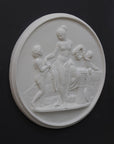 photo of white plaster cast relief sculpture of mostly nude female figure with two children and flowers and wreaths against dark gray background