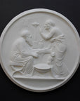 photo of white plaster cast relief sculpture of elderly male and female figures at a table and a cat against dark gray background