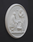 photo of white plaster cast relief sculpture of elderly male and female figures at a table and a cat against dark gray background