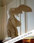 photo of plaster cast sculpture of winged, headless female figure with flowing drapery on top of a ribbed, square, wooden pedestal with white paneled walls behind