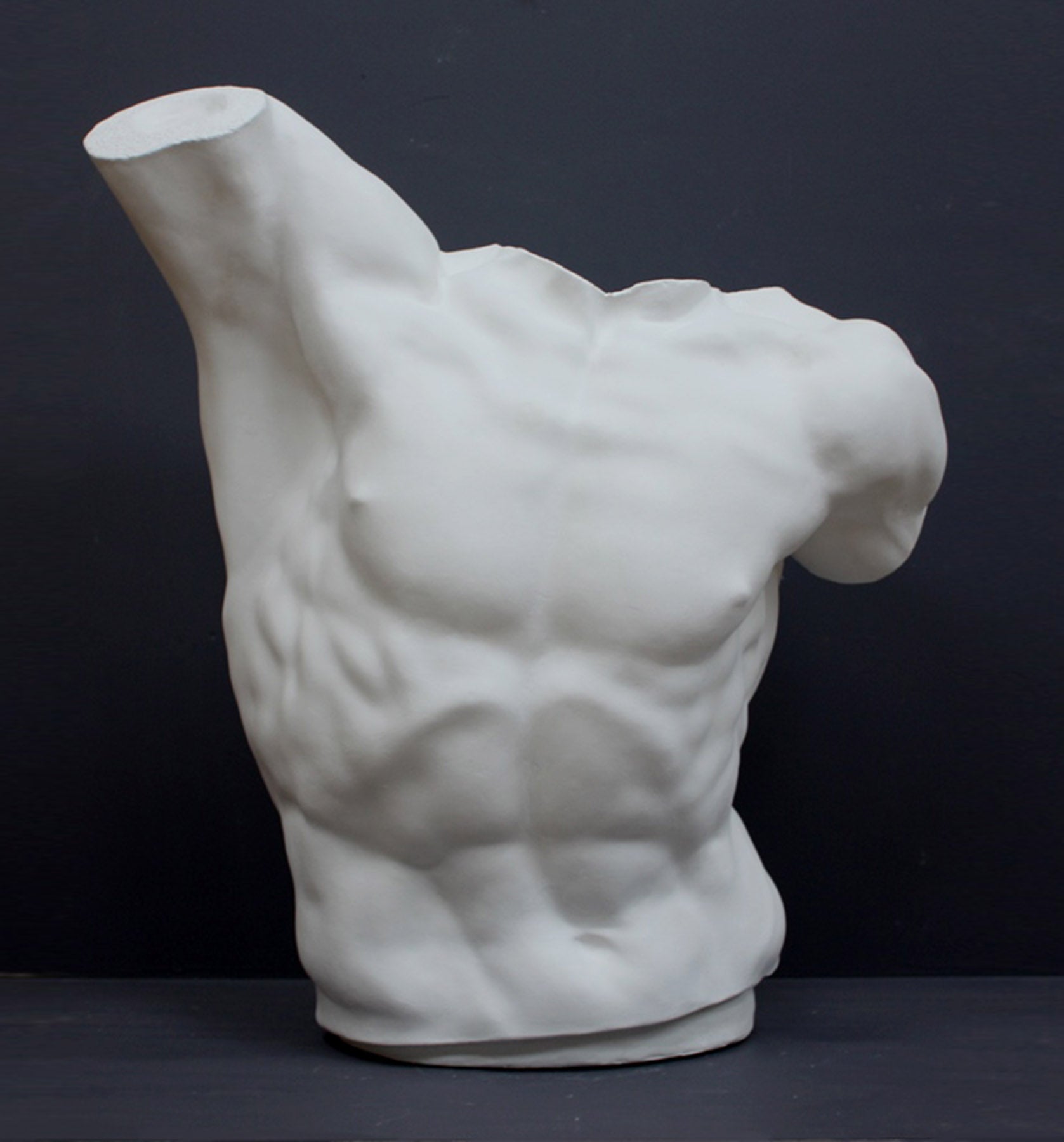 photo of white plaster cast sculpture of male torso, namely Laocoon, against gray background