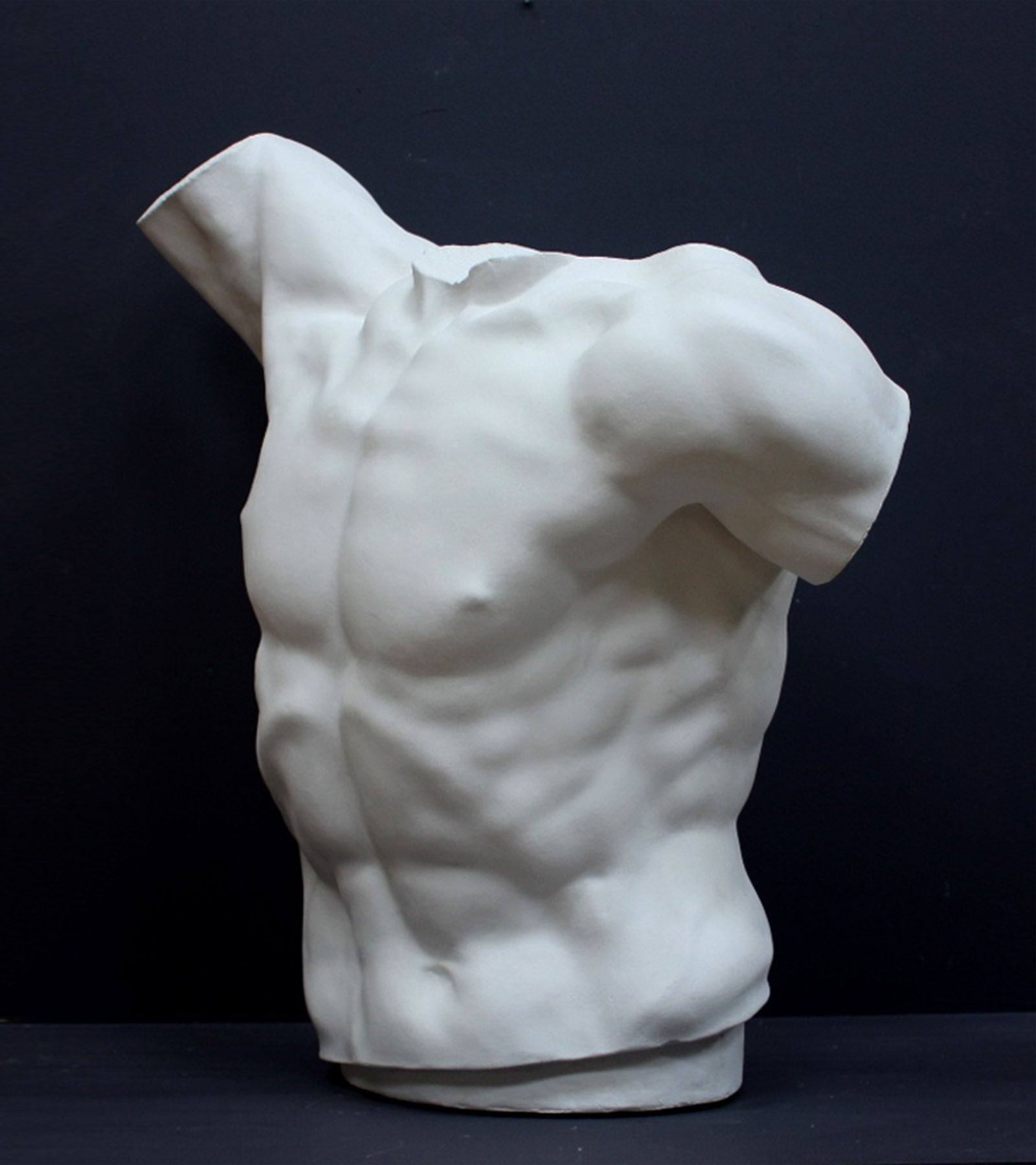 photo of white plaster cast sculpture of male torso, namely Laocoon, against gray background