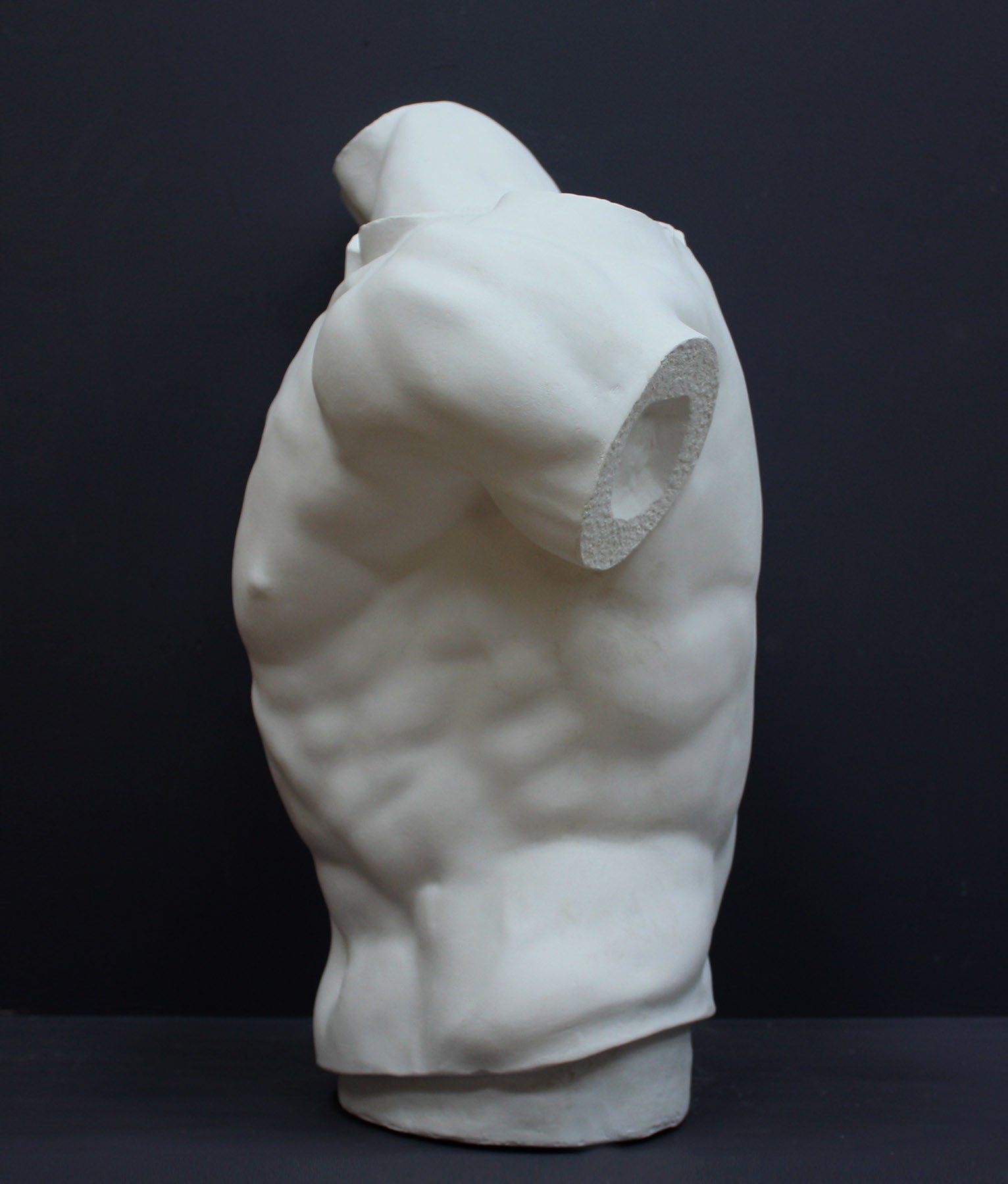 photo of white plaster cast sculpture of male torso, namely Laocoon, against gray background