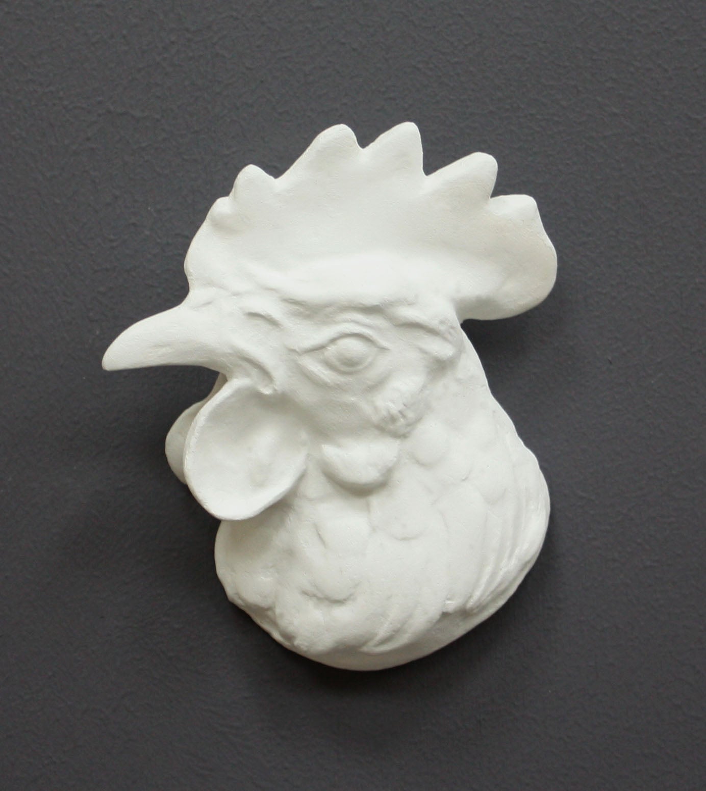 photo of white plaster cast sculpture of a rooster head facing to its right on gray background