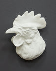 photo of white plaster cast sculpture of a rooster head facing to its right on gray background