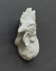 photo of white plaster cast sculpture of a rooster head facing to its right on gray background