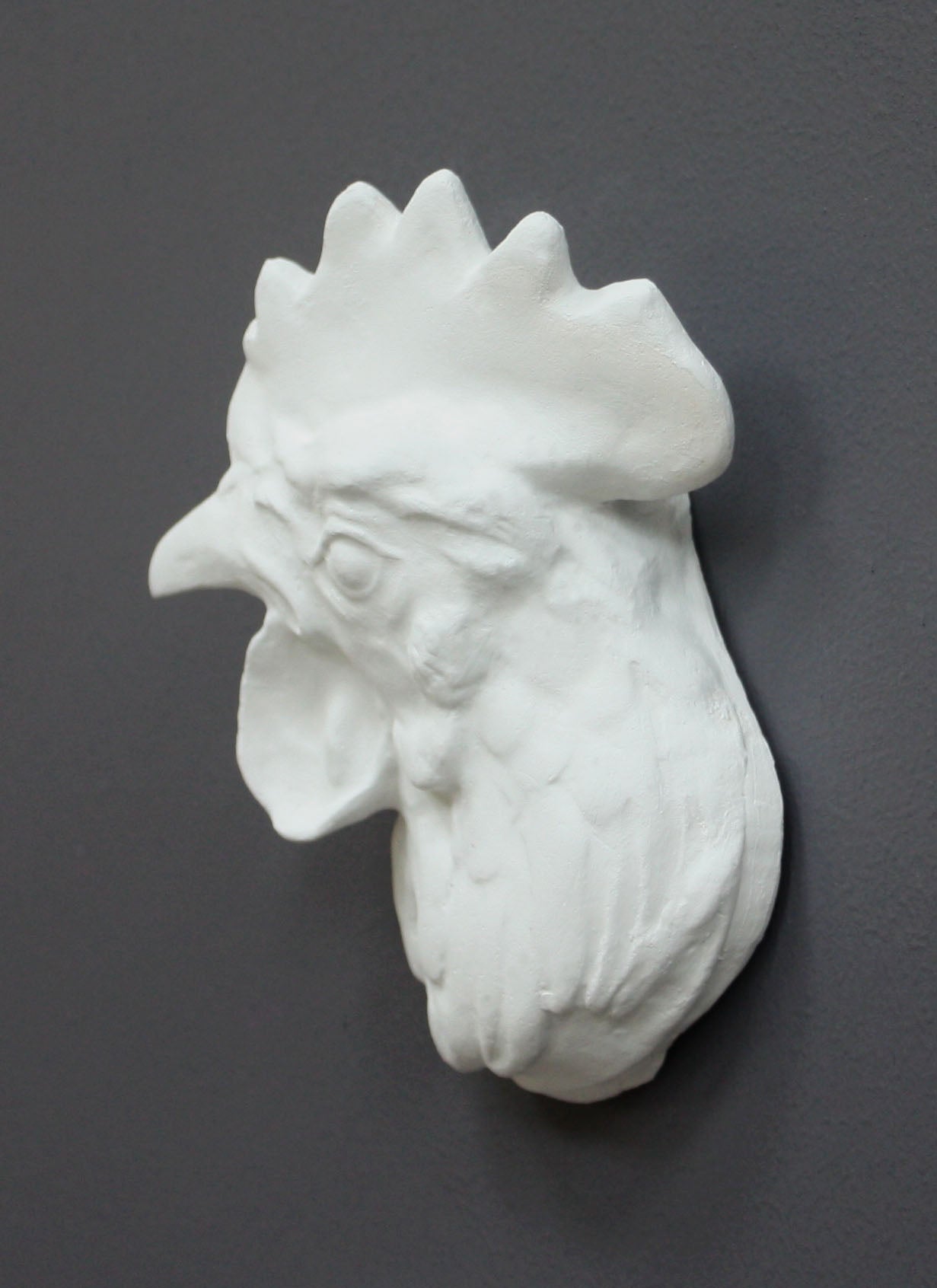 photo of white plaster cast sculpture of a rooster head facing to its right on gray background