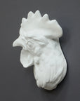 photo of white plaster cast sculpture of a rooster head facing to its right on gray background