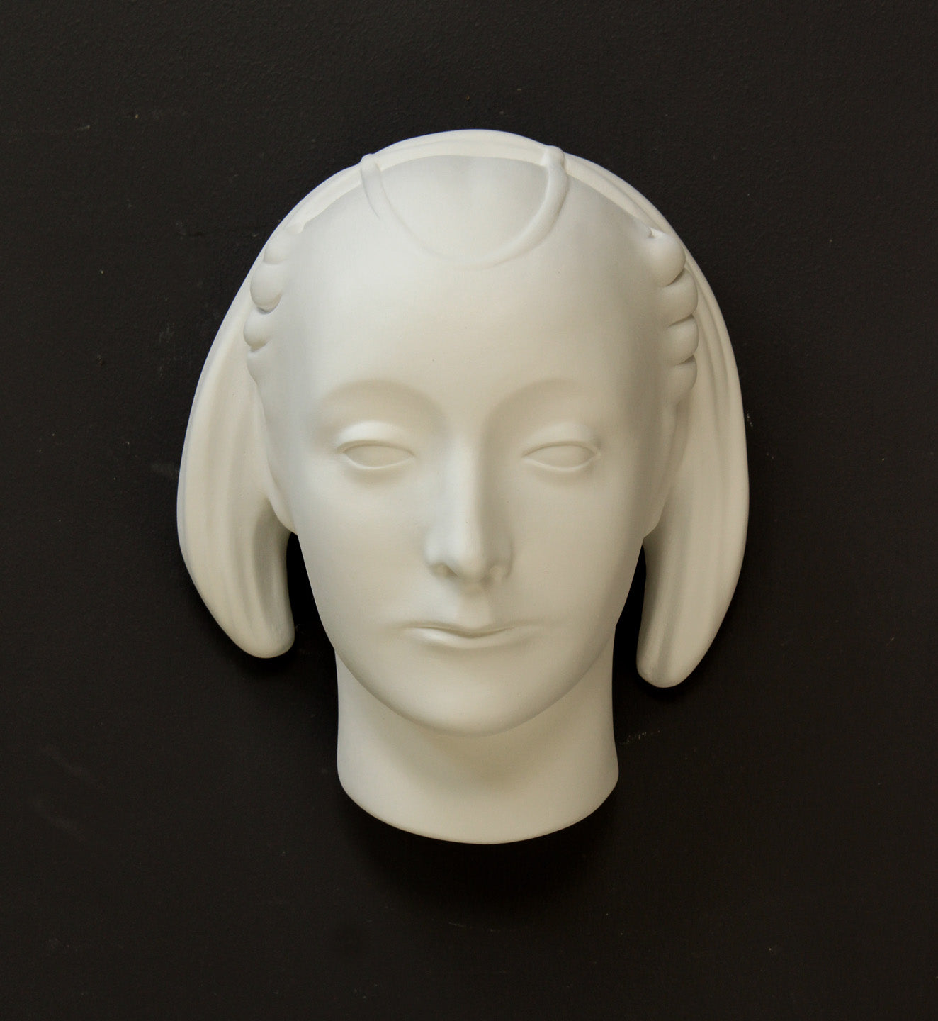 photo of white plaster cast sculpture mask of female with part-back hairdo against gray background