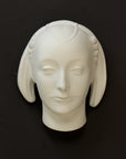 photo of white plaster cast sculpture mask of female with part-back hairdo against gray background