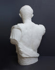 back view photo of white plaster cast sculpture of a man's torso with armor and robes with his right arm raised, namely Augustus Caesar, against a gray background