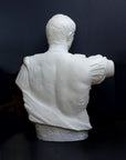 back view photo of white plaster cast sculpture of a man's torso with armor and robes with his right arm raised, namely Augustus Caesar, against a gray background