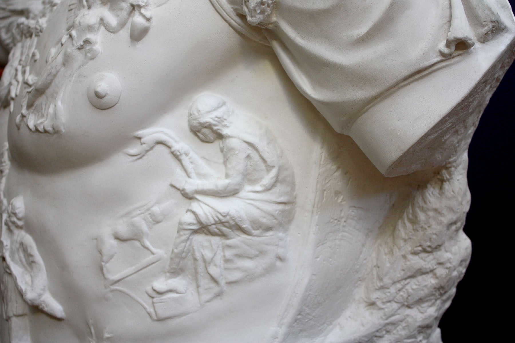 detail photo of armor from white plaster cast sculpture of a man&#39;s torso, namely Augustus Caesar, against a black background