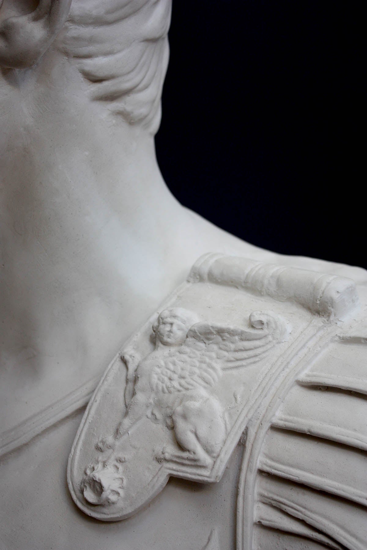 detail photo of armor from white plaster cast sculpture of a man&#39;s torso, namely Augustus Caesar, against a black background