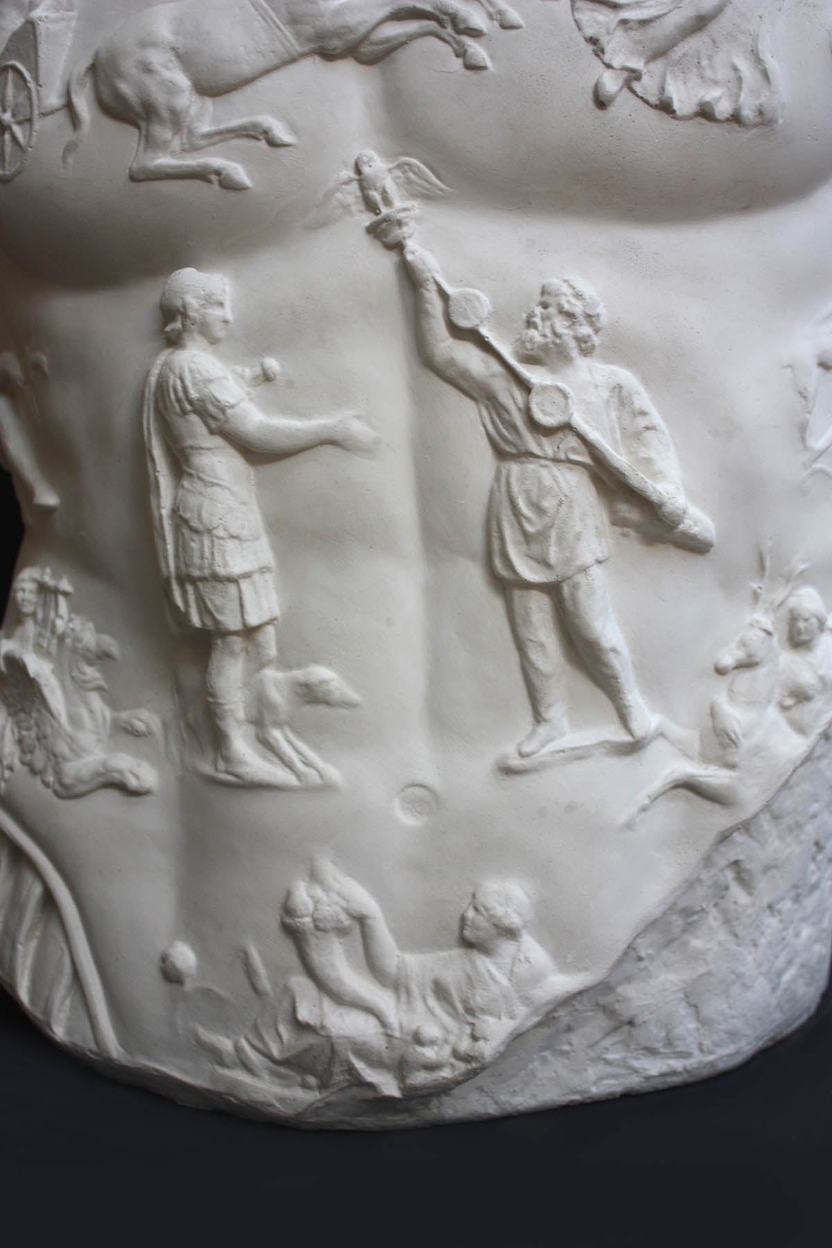 detail photo of armor from white plaster cast sculpture of a man&#39;s torso, namely Augustus Caesar, against a black background