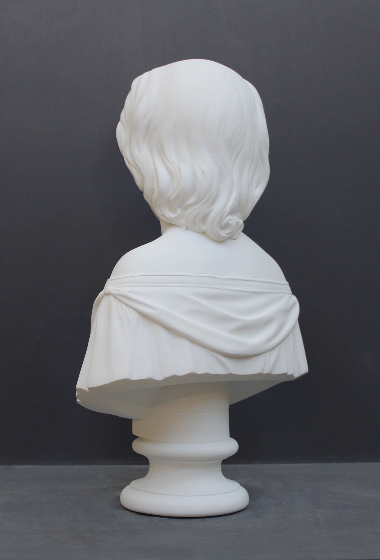 photo of white plaster cast bust sculpture of young woman with headband piece and in dress that falls off shoulders against a gray background