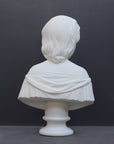 photo of white plaster cast bust sculpture of young woman with headband piece and in dress that falls off shoulders against a gray background