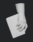 photo of white plaster cast of baby hand holding a book by the spine against gray background