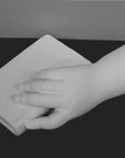 photo of white plaster cast of baby hand holding a book by the spine against gray background