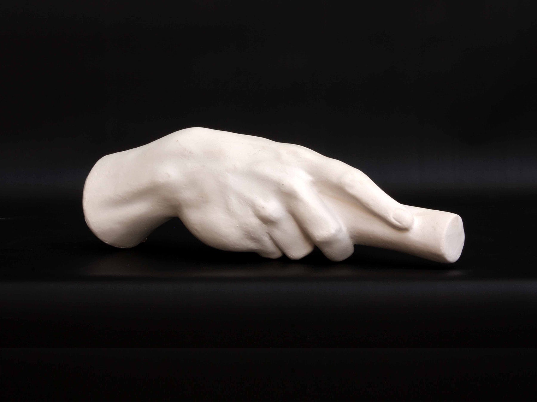 photo of white plaster cast of right hand grasping a staff or pole against black background