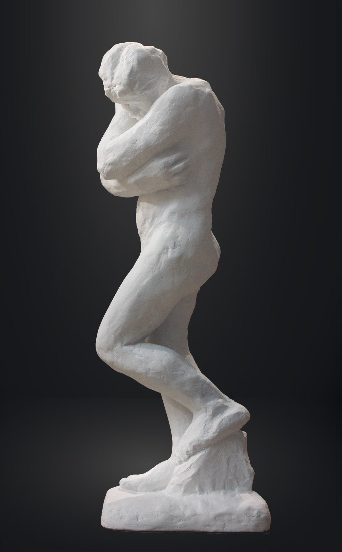 photo of white plaster cast sculpture of nude female figure hugging herself against gray background