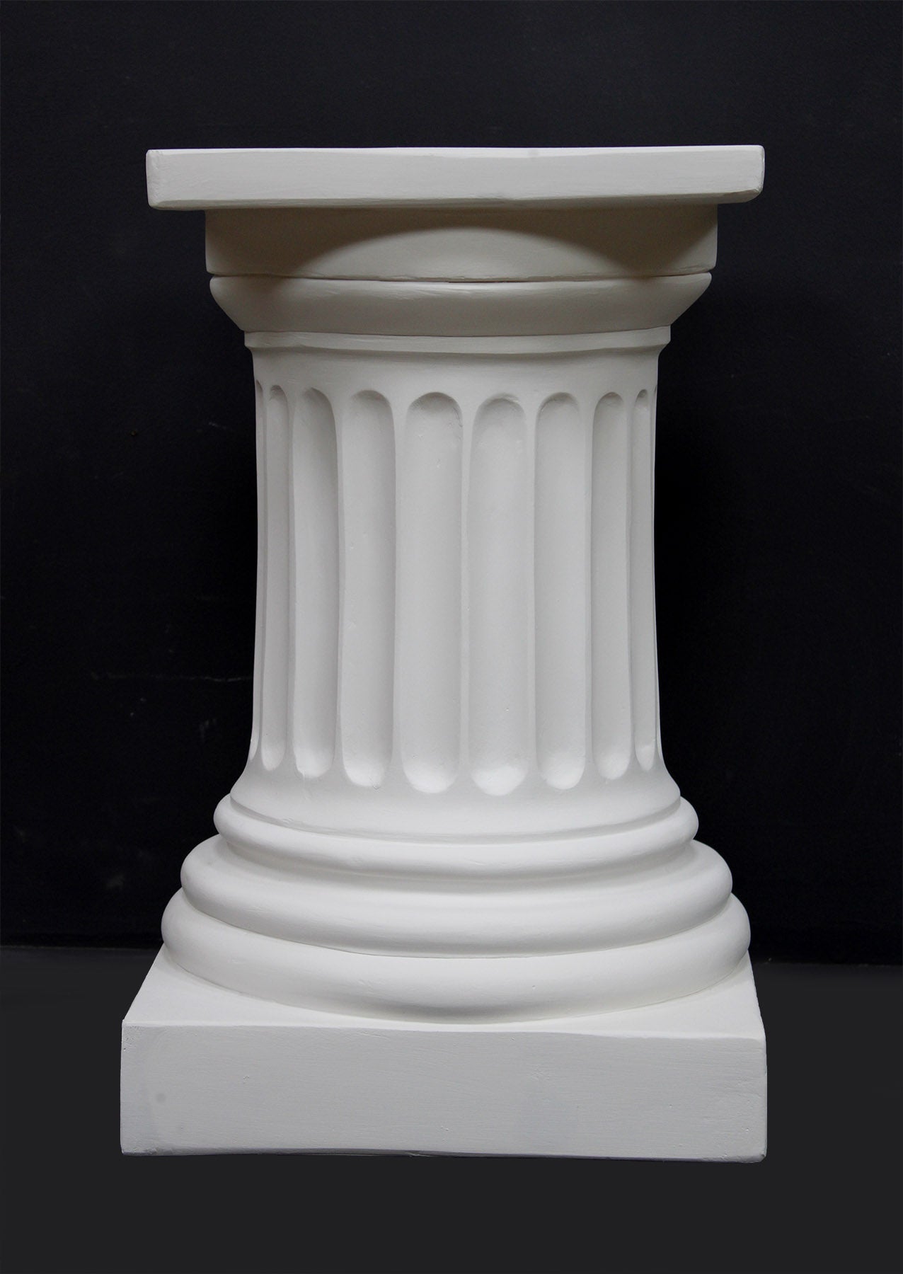 photo of short white plaster cast pedestal in the Doric style with a fluted column against a black background