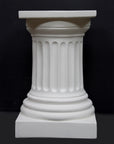 photo of short white plaster cast pedestal in the Doric style with a fluted column against a black background