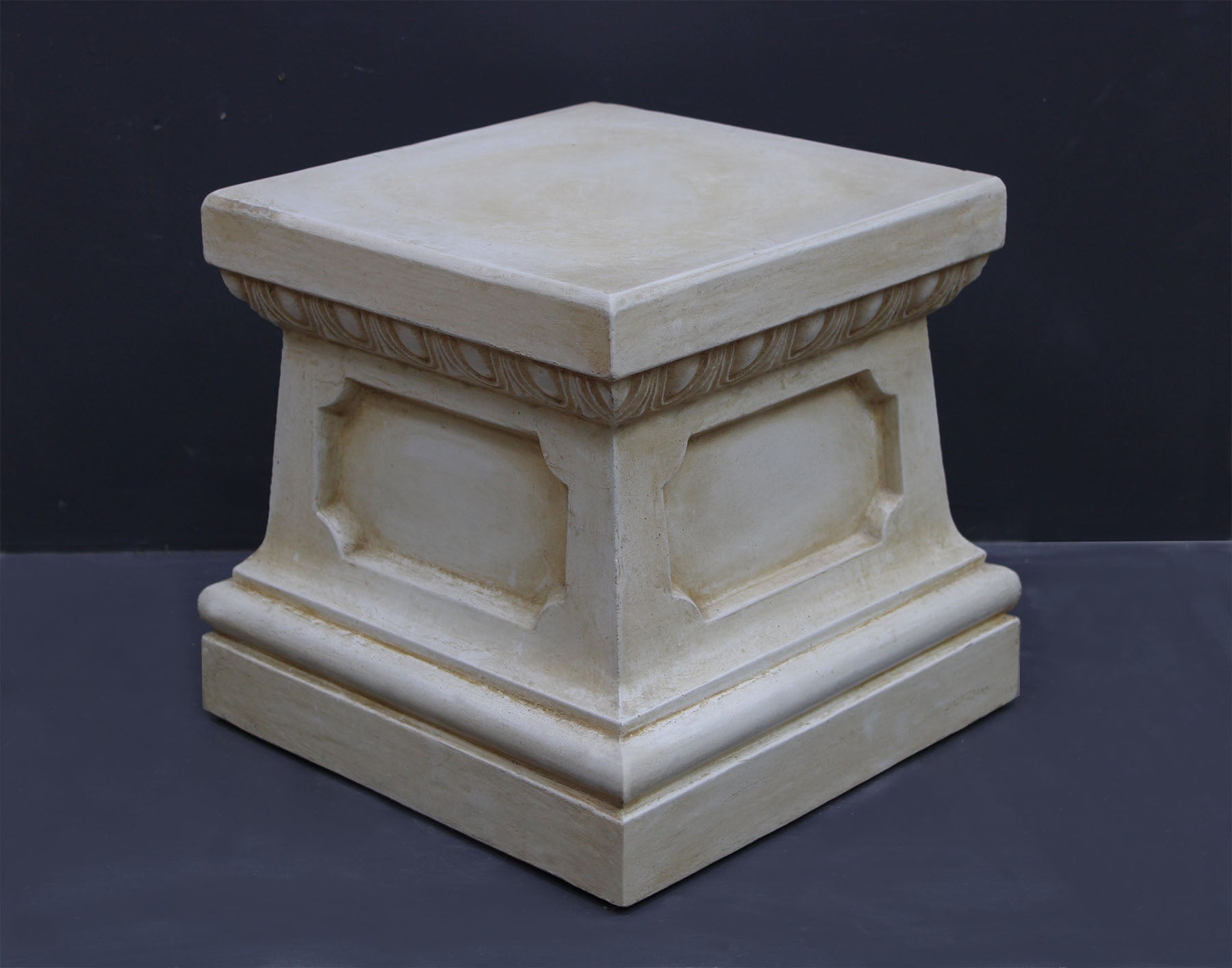 photo of off-white plaster cast reproduction of short, rectangular pedestal taken at an angle against a gray background