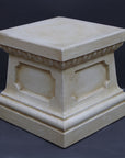 photo of off-white plaster cast reproduction of short, rectangular pedestal taken at an angle against a gray background