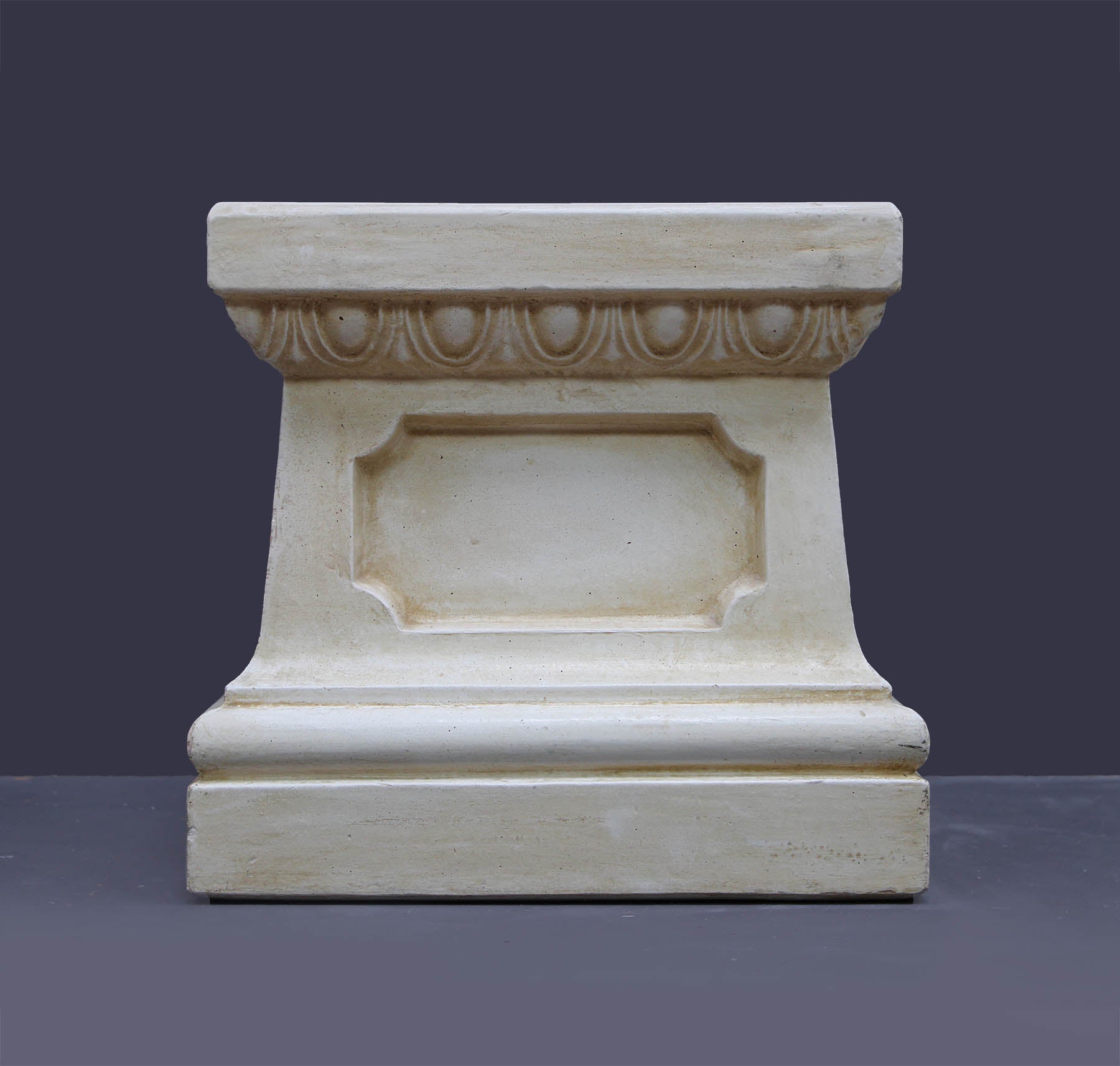 photo of off-white plaster cast reproduction of short, rectangular pedestal taken straight on and against a gray background