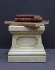 photo of off-white plaster cast reproduction of short, rectangular pedestal with three red books stacked on top against a gray background