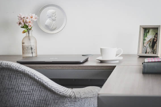 Photo of a white plaster cast of a medallion with a profile of a man wearing a wrath on his head, on a wall behind a desk with a vase, computer, coffee cup, and picture frame.