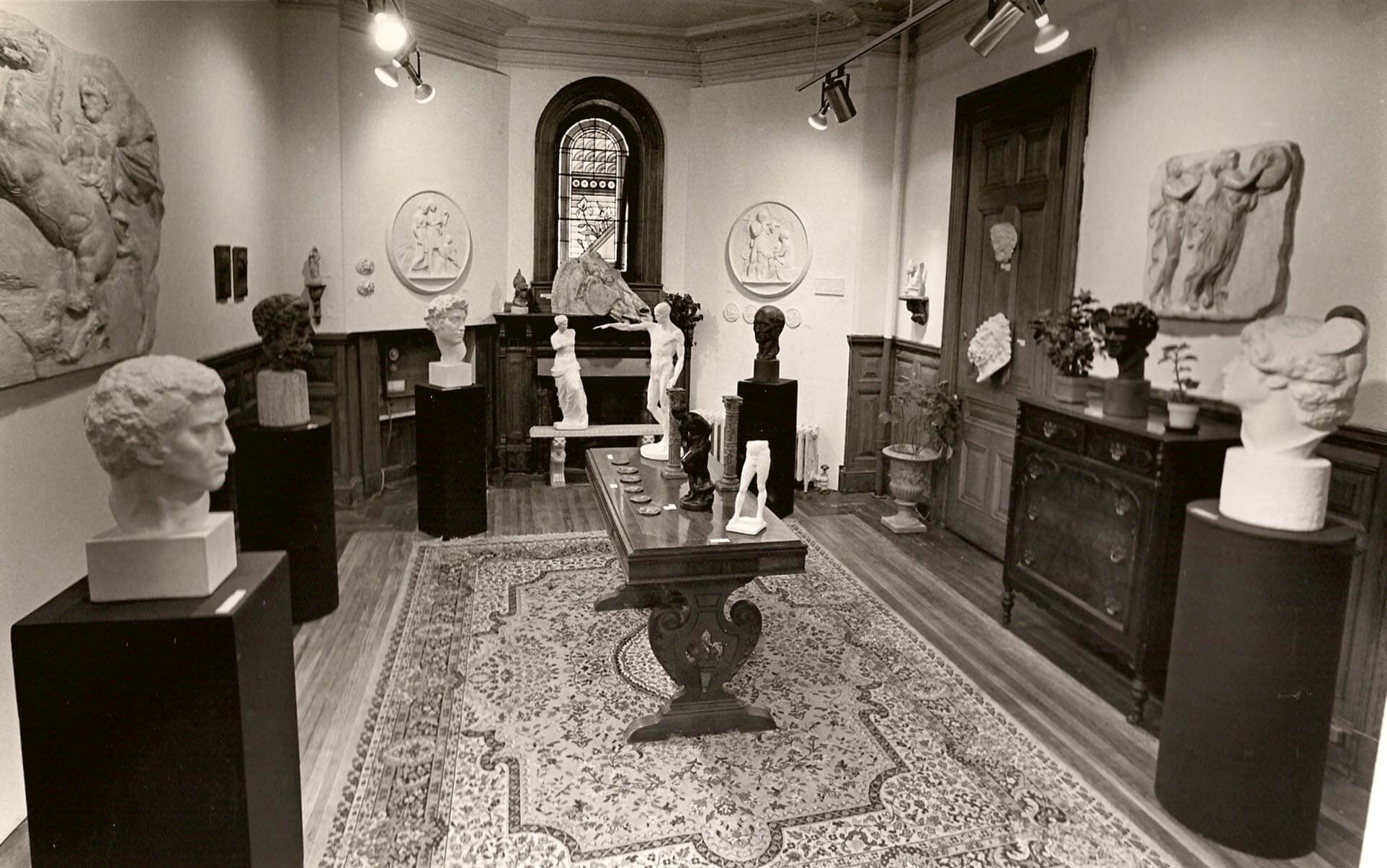 sepia photo of gallery with wood accents and furniture displaying plaster cast sculpture reproductions