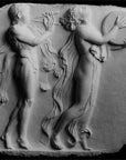 Photo of white plaster cast relief sculpture of two figures dancing in a procession against a black background