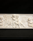 photo of white plaster cast with warm tones of relief sculpture of several cupids talking together with books and baskets of fruit on a black background