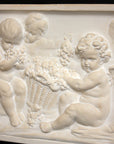 closeup photo of white plaster cast with warm tones of relief sculpture of several cupids talking together with books and baskets of fruit on a black background