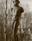 photo detail of bronze-colored plaster cast sculpture of standing nude satyr figure on square base in front of trees