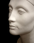 photo of plaster cast sculpture of bust of Nefertiti with crown and decorative collar on a decorative base with a black background