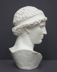 photo of white plaster cast sculpture bust of female, namely the goddess Athena, with short, curly hair and headband on gray background