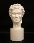 Photo of white plaster cast sculpture of faun head on base against black background