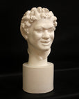 Photo of white plaster cast sculpture of faun head on base against black background