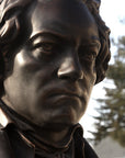 photo of bronze-colored plaster cast sculpture bust of man, namely Beethoven, with neckerchief with sky and trees in background