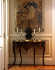 photo of bronze-colored plaster cast sculpture bust of man, namely Beethoven, with neckerchief on dark wood table with candlesticks and portrait painting behind