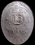 photo of white plaster reproduction of a shield with intricate relief sculpture set against black background