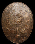 photo of bronze-colored plaster reproduction of a shield with intricate relief sculpture set against black background