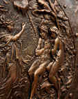 detail photo of bronze-colored plaster reproduction of a shield with intricate relief sculpture set against black background