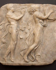 Photo of stone-colored plaster cast relief sculpture of two figures dancing in a procession against a black background